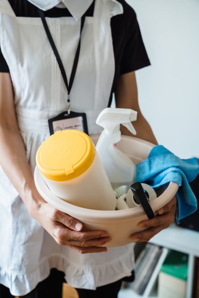 A uniformed cleaner holding a basin with cleaning supplies indoors. Ideal for cleaning and sanitation themes.